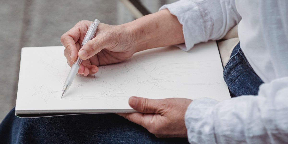 A person immersed in drawing in a notebook, illustrating the calming and expressive power of creative self-care.